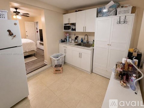 A kitchen with white cabinets and appliances, a bed, and a fan.