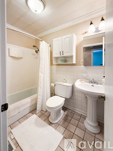 A white toilet sits in a bathroom next to a sink and a bathtub.