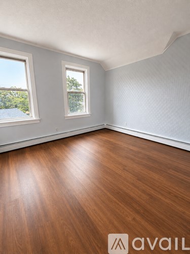A room with wooden flooring and two windows.