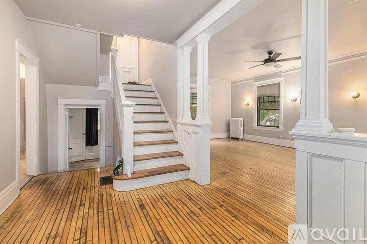 A spacious room with wooden floors and a staircase leading to another level.