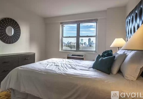 A bedroom with a large bed, a window with a view of the city, and a lamp on the bedside table.