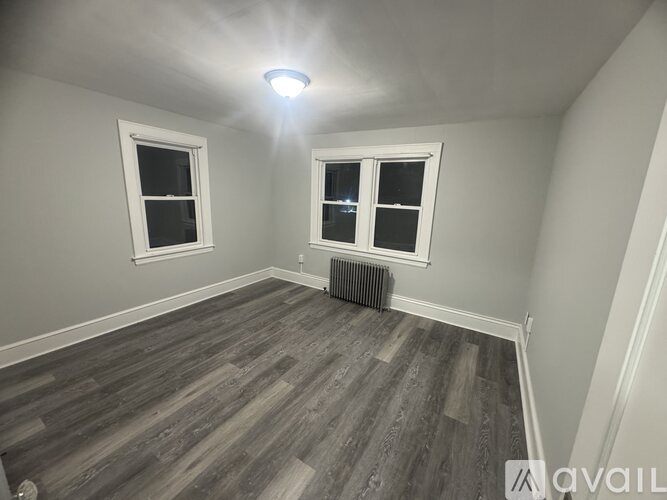 A room with wooden flooring and two windows.