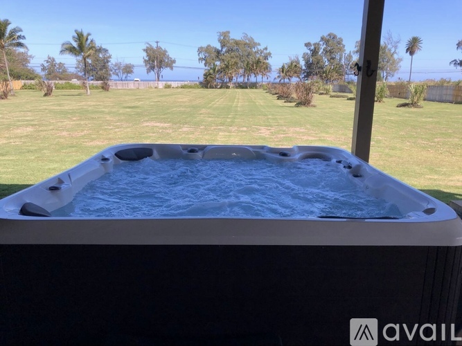 A hot tub is in the foreground with a view of a grassy field and trees in the background.