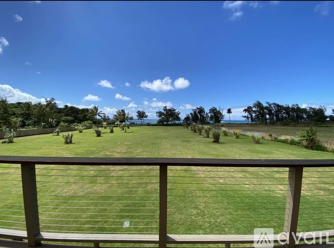A view from a balcony overlooking a green lawn and trees.