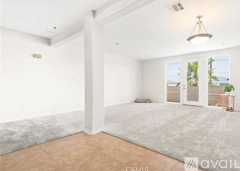 A spacious living room with a large window and a grey rug on the floor.