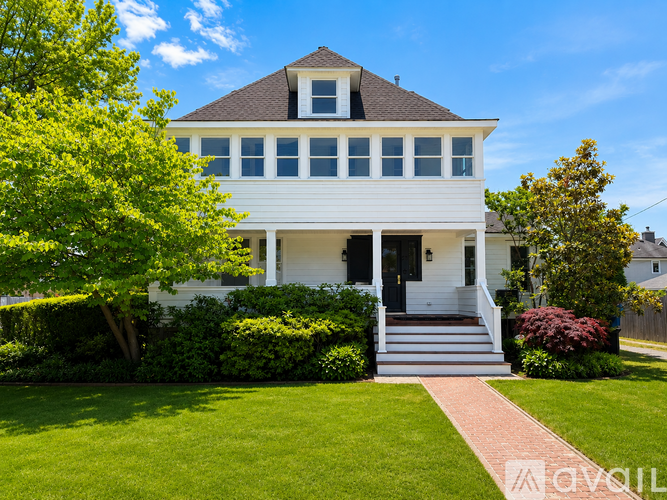 A white house with a black door and windows is surrounded by greenery.