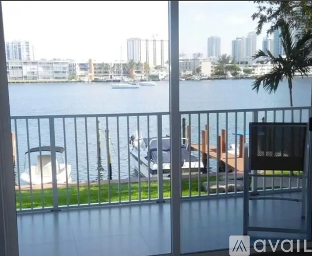 A balcony with a metal railing overlooks a body of water with boats and buildings in the distance.
