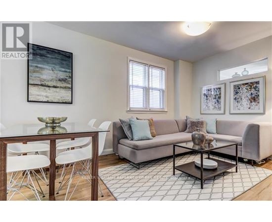 A living room with a grey couch, a glass table, and a painting on the wall.