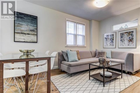 A living room with a grey couch, a glass table, and a painting on the wall.