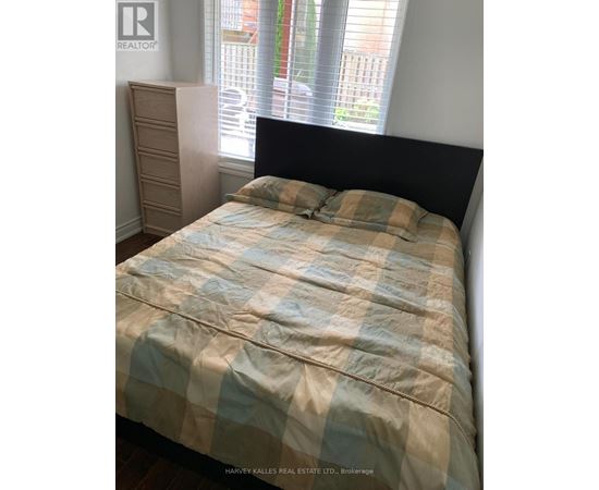 A bed with a blue and beige comforter is in a room with a window.