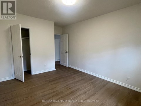 A room with a wooden floor and white walls, with a door open to another room.