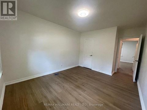 A room with wooden flooring and white walls, with a doorway leading to another room.