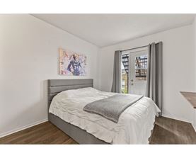 A bedroom with a bed, a painting on the wall, and a window with curtains.