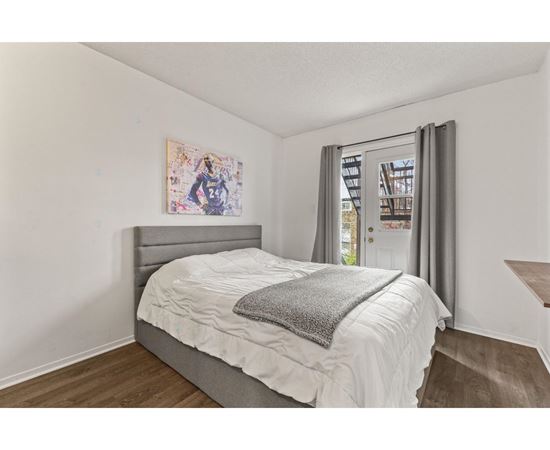 A bedroom with a bed, a painting on the wall, and a window with curtains.