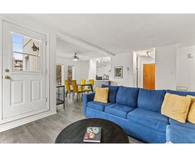 A blue couch with yellow pillows is in the foreground of a bright living room.