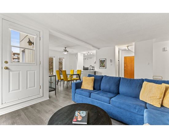 A blue couch with yellow pillows is in the foreground of a bright living room.