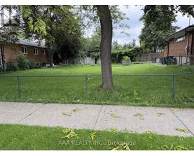 A tree in a grassy area with a fence and houses in the background.