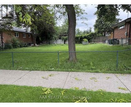 A tree in a grassy area with a fence and houses in the background.
