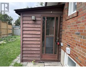A brown wooden shed with a glass door is situated next to a brick wall.