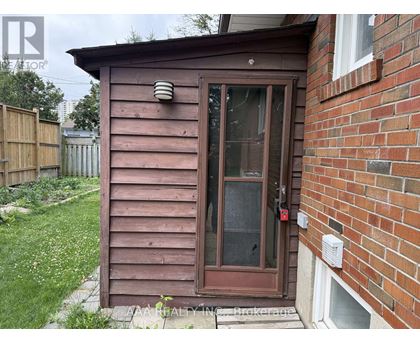 A brown wooden shed with a glass door is situated next to a brick wall.