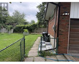 A backyard with a fence, a trash can, and a hose.