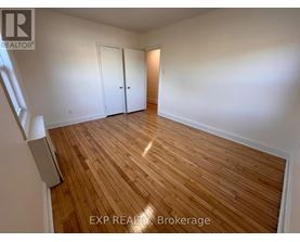 A room with wooden flooring and white walls, with a window on the left side.
