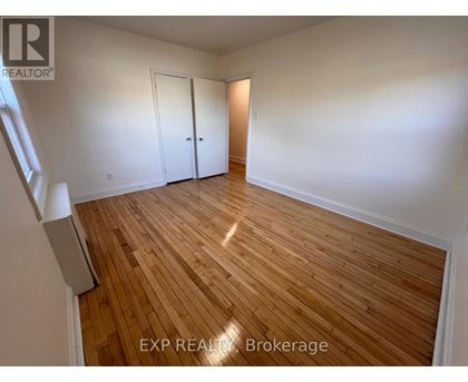 A room with wooden flooring and white walls, with a window on the left side.