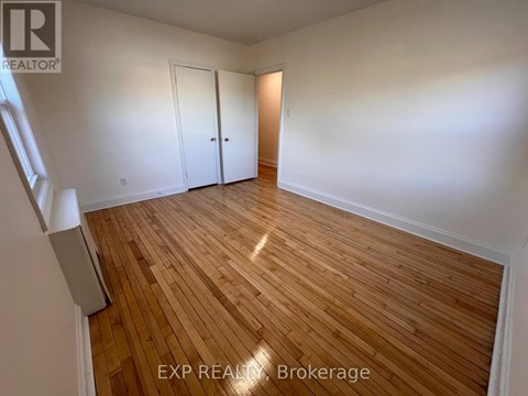 A room with wooden flooring and white walls, with a window on the left side.