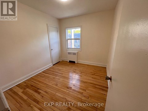 A room with wooden flooring and a window with a view of a building outside.