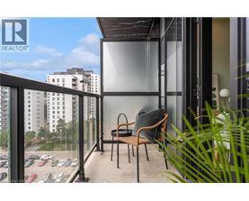 A balcony with a chair and a pillow with a view of a parking lot and buildings.
