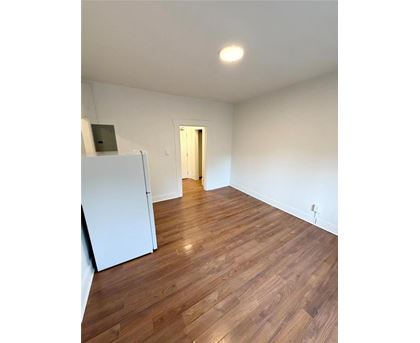 A room with wooden flooring and a white refrigerator.