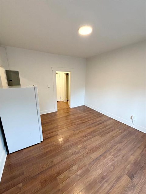 A room with wooden flooring and a white refrigerator.