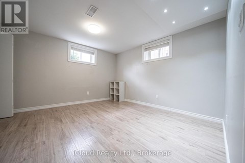 A room with wooden flooring and two windows.