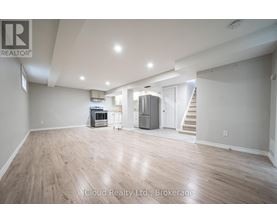 A spacious room with wooden flooring and a staircase in the background.