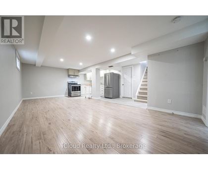 A spacious room with wooden flooring and a staircase in the background.