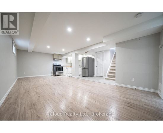 A spacious room with wooden flooring and a staircase in the background.