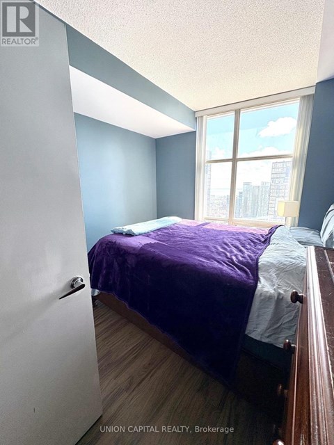 A bedroom with a purple bedspread and a window showing a cityscape.
