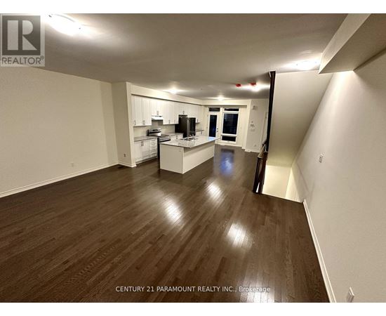A spacious room with wooden flooring and white walls, featuring a kitchen area with white cabinets and appliances.