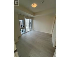 A spacious room with wooden flooring and a sliding glass door leading to a balcony.