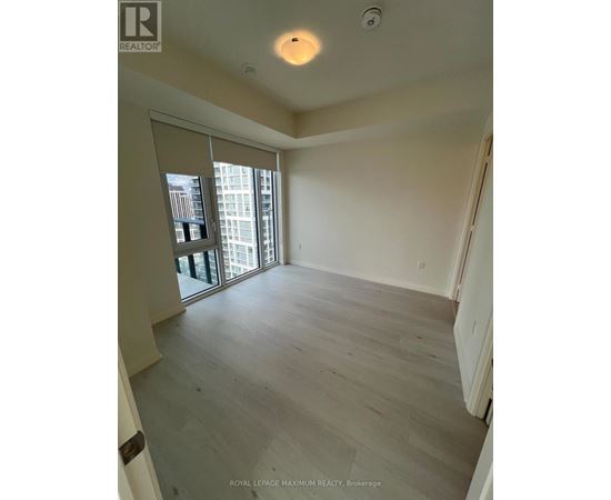 A spacious room with wooden flooring and a sliding glass door leading to a balcony.