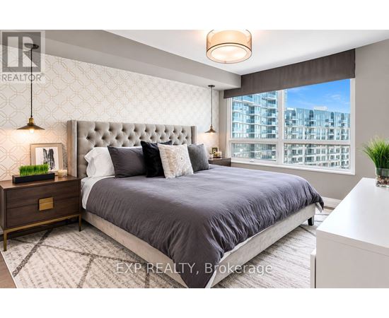 A bedroom with a large bed, a nightstand with a lamp, and a window with a view of a building.