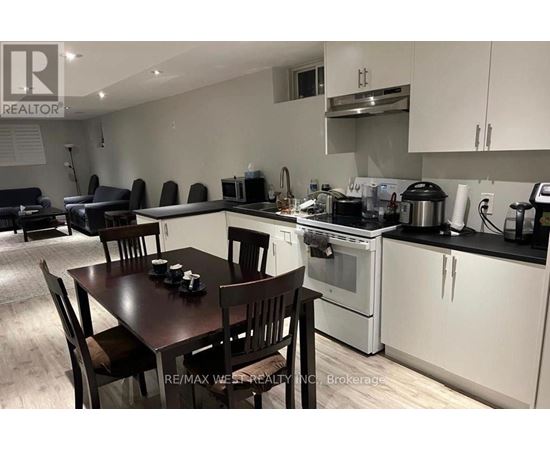 A kitchen with a table and chairs in the foreground and a stove top oven in the background.