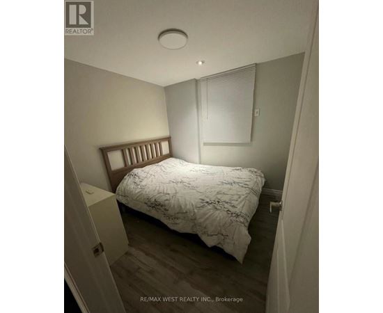 A bedroom with a bed, nightstand, and window with blinds.