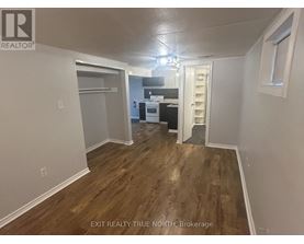 A room with wood flooring and a kitchen area in the background.