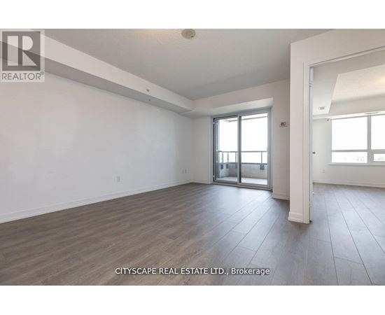 A spacious room with wooden flooring and a sliding glass door.