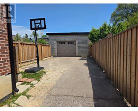A basketball hoop stands in the middle of a driveway leading to a garage.