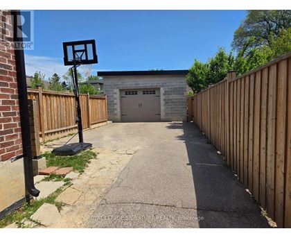 A basketball hoop stands in the middle of a driveway leading to a garage.