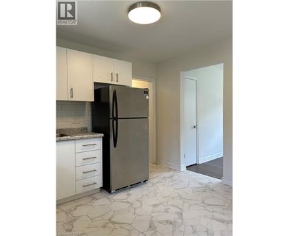 A kitchen with a refrigerator, cabinets, and a marble floor.