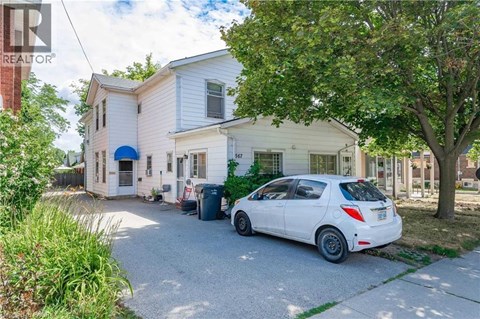 A white car is parked in front of a two-story house.