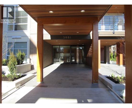 The image shows a modern building entrance with a wooden roof and glass doors.